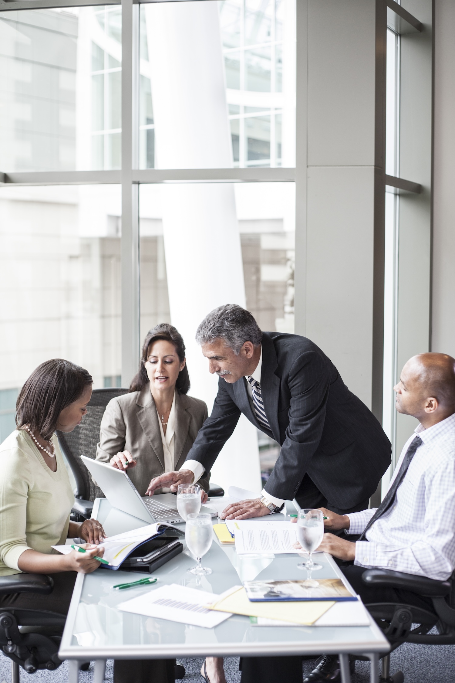 A mixed race group of male and female business people in a meeting at a conference table next to a large window in a convention center.